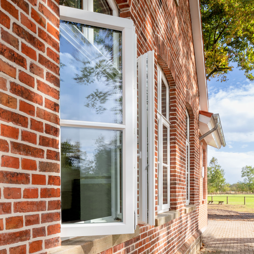Geöffnete weiße Fenster in einem Ziegelsteinhaus.
