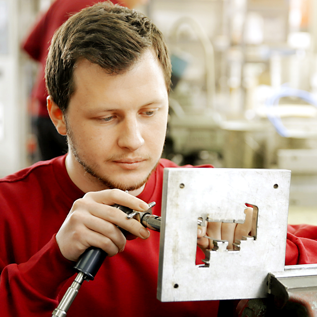 Ein Stöckel Mitarbeiter arbeitet konzentriert an einem Extrusionsstück.