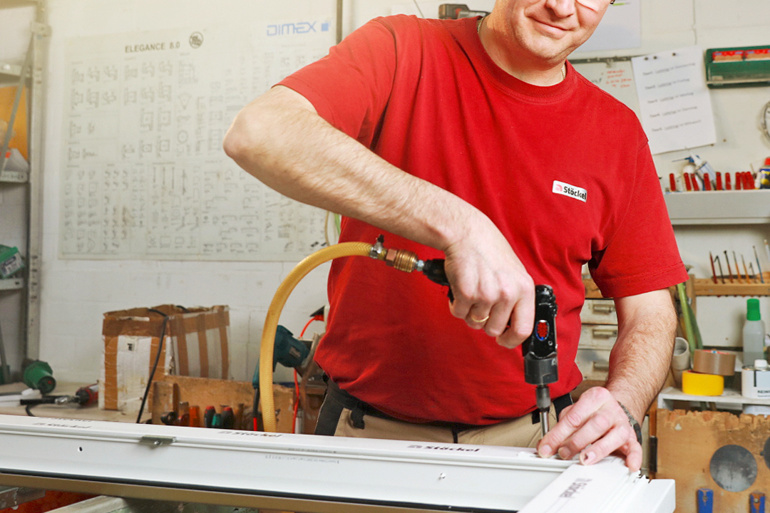 Ein Stöckel Mitarbeiter in rotem T-Shirt bearbeitet ein weißes Kunststofffenster.