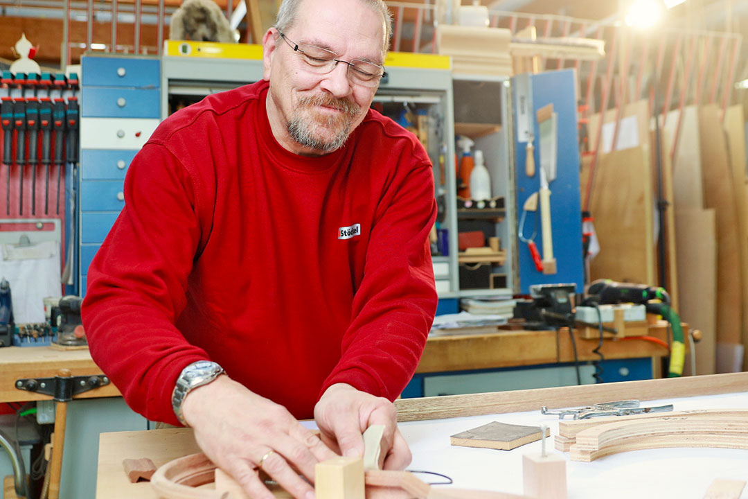 Ein sympathisch lächelnder Stöckel Mitarbeiter arbeitet an Holzelementen.