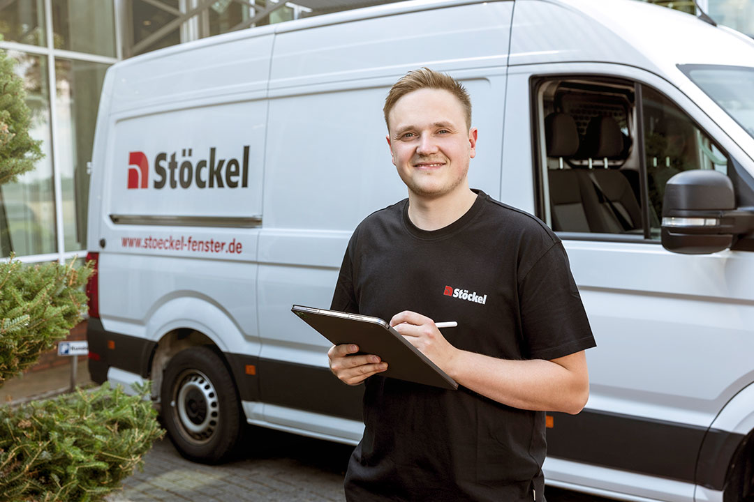 Ein Stöckel Mitarbeiter steht lächelnd vor seinem Transporter.