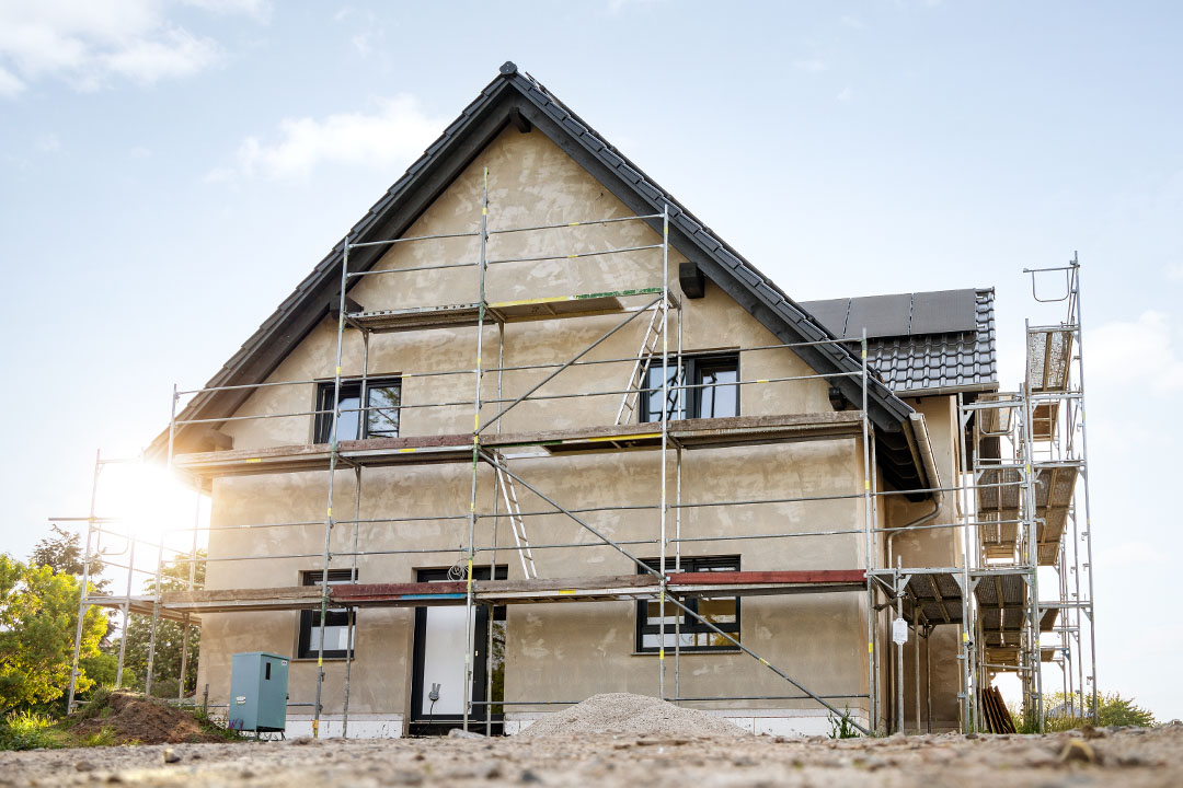 Ein eingerüstetes Rohbau-Haus mit Fenstern und Haustür.